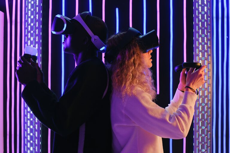 Two people stand back to back, each with a VR headset and controllers