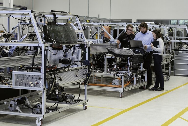 A picture of an automotive factory showing three people working on a highly technical product.
