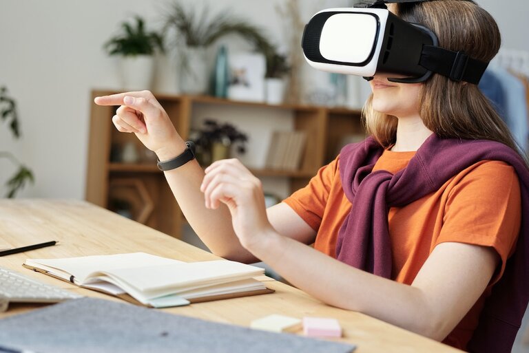 A person wearing a virtual reality headset. The person is making gestures and sitting in front of a book.